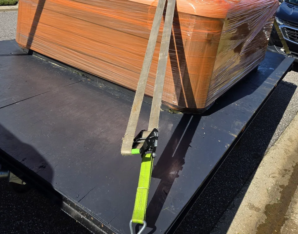 Wrapped hot tub on a trailer with a tie-down in the foreground.
